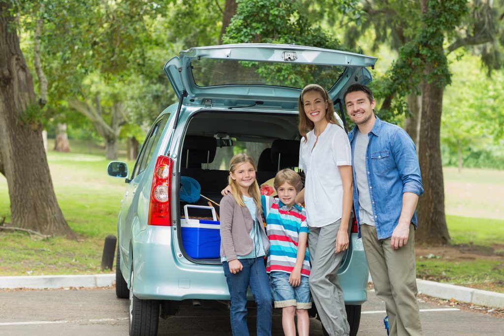 Portrait of a happy family of four by car trunk while on picnic